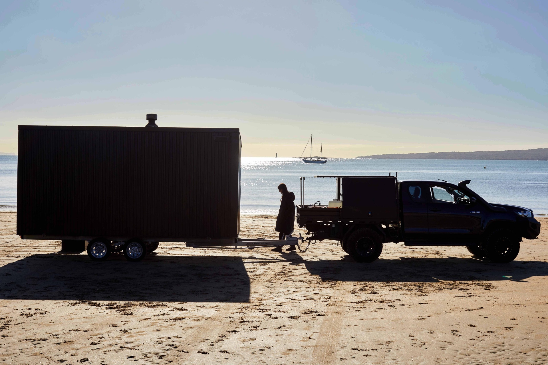 The mobile sauna being towed along the beach at sunrise