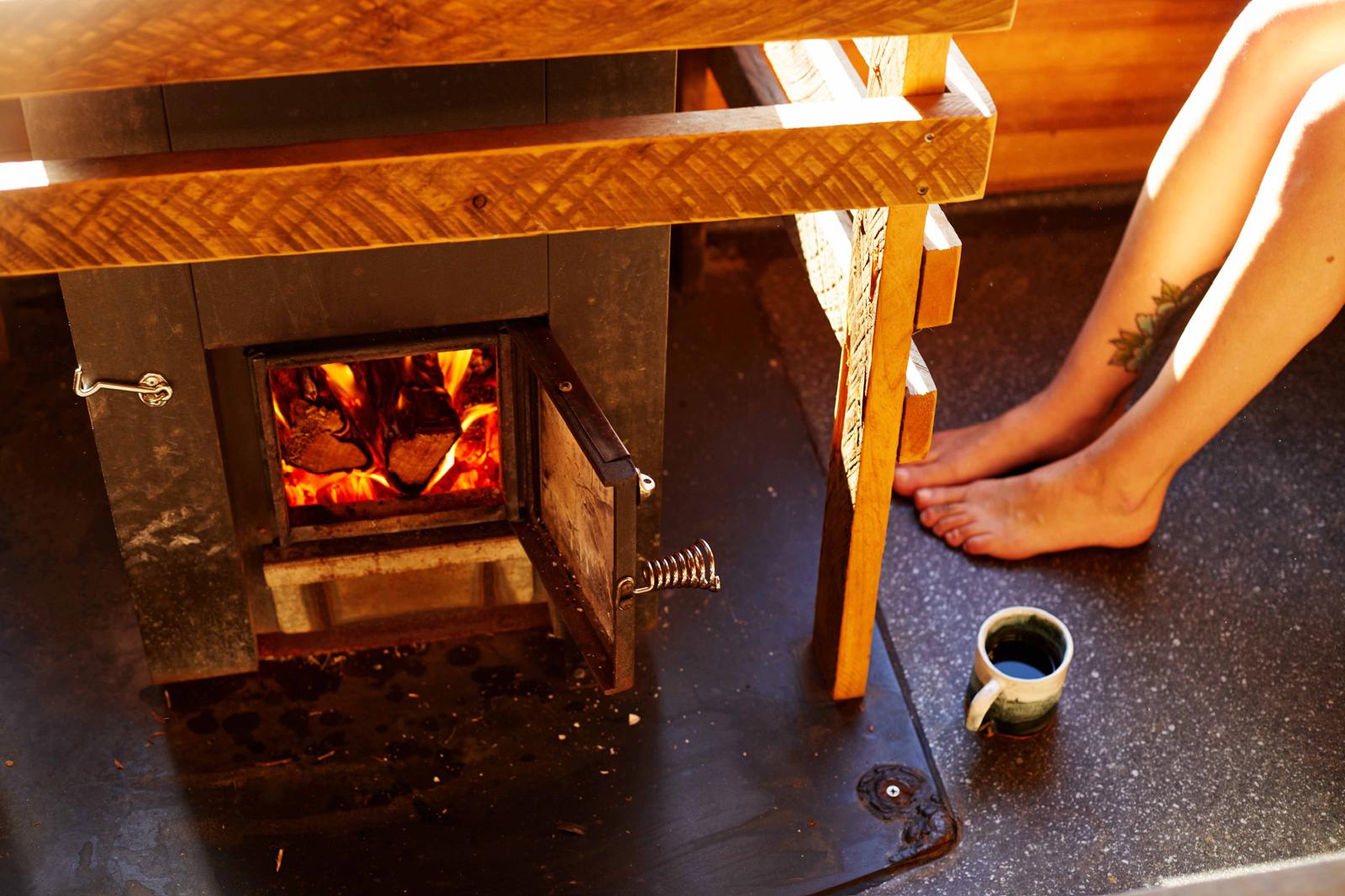 Bare feet resting by the glowing wood-fired stove with a cup of tea